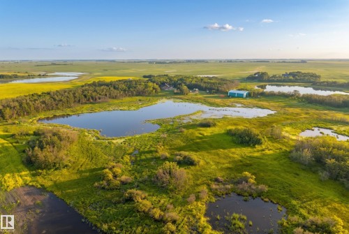 Expansive agricultural landscape featuring multiple bodies of water, diverse foliage, and a large blue-roofed structure - 48109 Rr 155, Rural Beaver County, AB - Outdoor With View