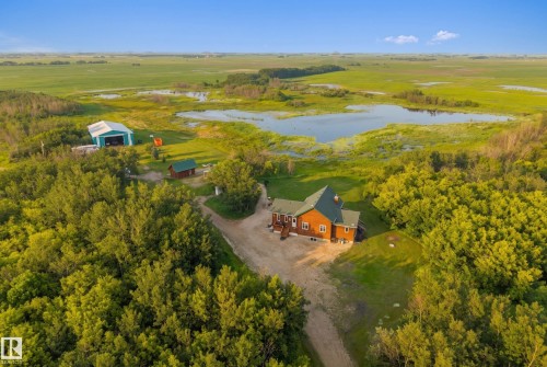 Expansive property featuring a brown-sided residence with green roofing, a large blue barn, a smaller green outbuilding, and a pond - 48109 Rr 155, Rural Beaver County, AB - Outdoor With View