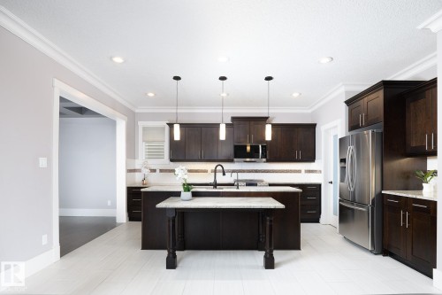 Kitchen featuring dark wood cabinetry, stainless steel appliances, a center island with a granite countertop, pendant lighting, and light-toned wood-finish flooring - 886 Armitage Wynd Sw, Edmonton, AB 