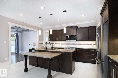 Kitchen featuring dark wood-finish cabinetry, stainless steel appliances, pendant lighting, recessed lighting, and a kitchen island with an extended granite countertop - 886 Armitage Wynd Sw, Edmonton, AB 