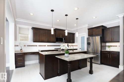 Kitchen featuring dark wood-finish cabinetry, white countertops, tile backsplash, and stainless steel appliances - 886 Armitage Wynd Sw, Edmonton, AB 