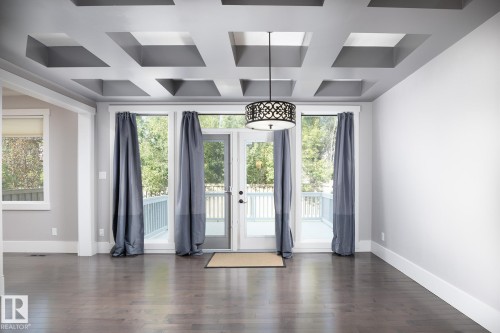 Coffered ceiling with recessed panels, wood-finish flooring, and French doors opening to an outdoor deck - 886 Armitage Wynd Sw, Edmonton, AB 
