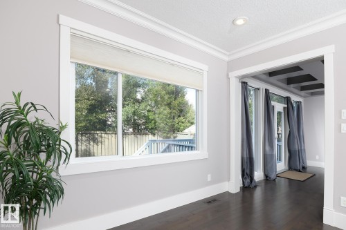 Expansive window with bright trim, dark wood-finish flooring, recessed lighting, and a coffered ceiling visible through a wide doorway - 886 Armitage Wynd Sw, Edmonton, AB 