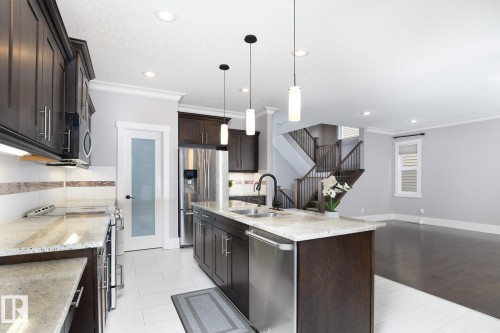 Kitchen featuring dark wood cabinetry, light countertops, stainless steel appliances, a center island with sink, and pendant lighting - 886 Armitage Wynd Sw, Edmonton, AB 