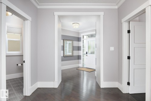 Dark wood-finish flooring, white trim, recessed lighting, white interior doors with black hardware, and a front entry door with glass panels - 886 Armitage Wynd Sw, Edmonton, AB 