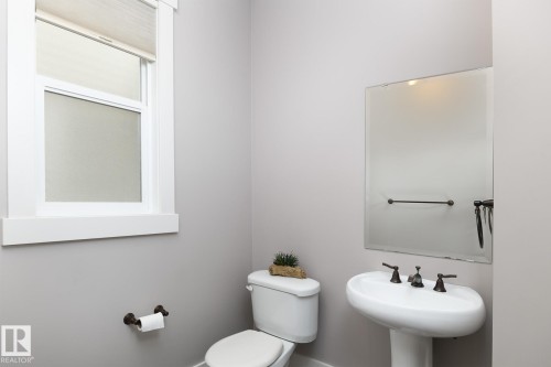 Pedestal sink with bronze-finish fixtures, coordinating toilet, and a framed mirror - 886 Armitage Wynd Sw, Edmonton, AB 