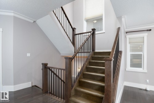 Staircase with wood-finish newel posts and railings, black metal balusters, and carpeted treads - 886 Armitage Wynd Sw, Edmonton, AB 