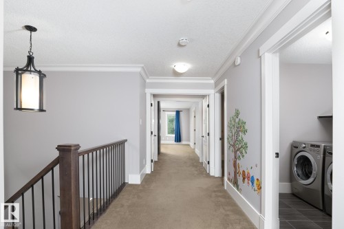 Hallway with carpet flooring, crown molding, and a dark wood and metal stair railing - 886 Armitage Wynd Sw, Edmonton, AB 