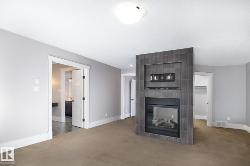 Tile-surround fireplace with an integrated media niche, wall-to-wall carpeting, light gray wall paint, white trim, and a flush-mount ceiling light - 886 Armitage Wynd Sw, Edmonton, AB 