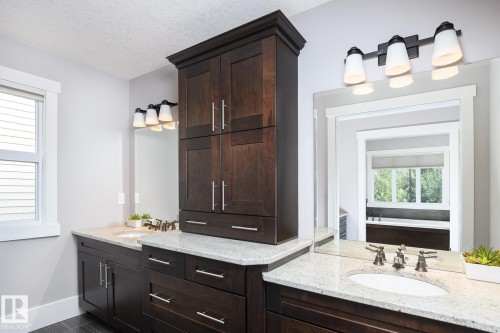 Dual sink vanity with stone countertops, dark wood cabinetry, and brushed bronze fixtures - 886 Armitage Wynd Sw, Edmonton, AB 