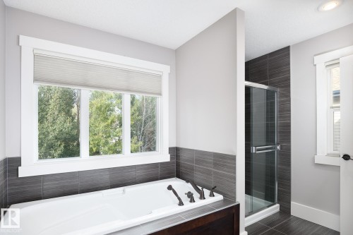 Built-in soaking tub with dark finish surround, bronze-finish fixtures, and a large window - 886 Armitage Wynd Sw, Edmonton, AB 
