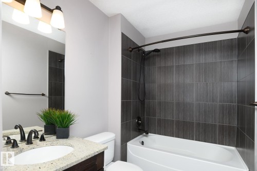 Granite-style countertop with an oval undermount sink, dark wood-finish vanity, and bronze-finish fixtures - 886 Armitage Wynd Sw, Edmonton, AB 