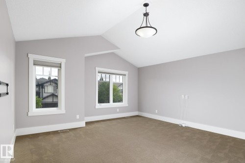 Vaulted ceiling with a pendant light fixture, two windows with white trim, light gray painted walls, and neutral-toned carpeting - 886 Armitage Wynd Sw, Edmonton, AB 