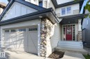 Stone accent facade with siding, two-car garage with transom windows, covered entry with a red door, and multiple windows - 886 Armitage Wynd Sw, Edmonton, AB 