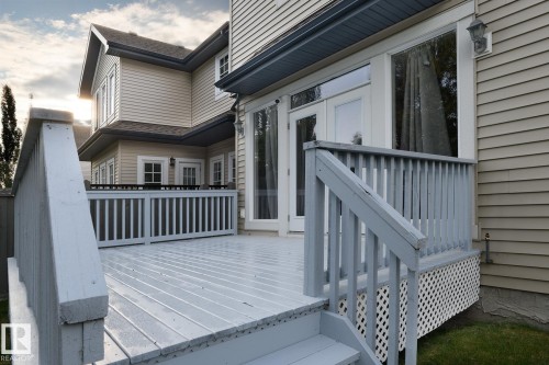 Expansive outdoor deck with painted railing and lattice skirting, featuring direct access via a double glass door, integrated exterior lighting, and wood-style siding - 886 Armitage Wynd Sw, Edmonton, AB 