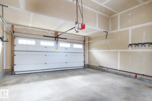 Attached garage featuring a concrete floor, automatic garage door opener, and upper transom windows - 886 Armitage Wynd Sw, Edmonton, AB 