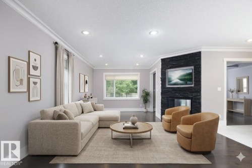 Spacious living area featuring dark wood-finish flooring, recessed lighting, crown molding, and a corner fireplace with a dark stone-finish surround - 886 Armitage Wynd Sw, Edmonton, AB 