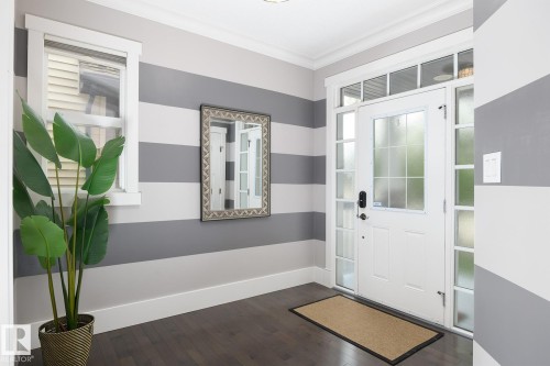 Entryway featuring a white paneled door with frosted glass inserts, coordinating sidelights, a transom window, and dark wood-finish flooring - 886 Armitage Wynd Sw, Edmonton, AB 