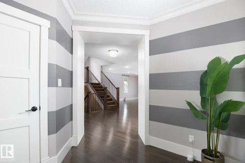Wood-finish flooring throughout, bright white trim, paneled interior doors with matte black hardware, and a staircase featuring wood risers and railings - 886 Armitage Wynd Sw, Edmonton, AB 