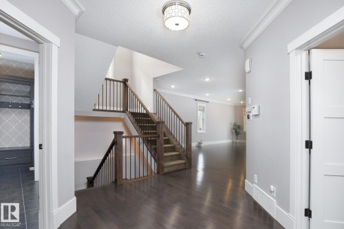 Hardwood flooring throughout the main level, a grand staircase with dark wood banisters and metal spindles, recessed lighting, and a built-in mudroom area with patterned tile flooring - 886 Armitage Wynd Sw, Edmonton, AB 
