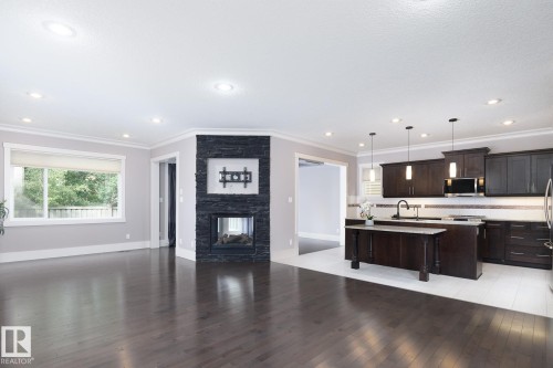 Hardwood-finish flooring, recessed lighting, and a corner fireplace with a dark stone surround - 886 Armitage Wynd Sw, Edmonton, AB 