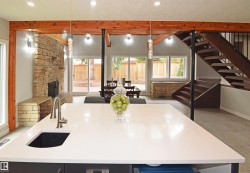 Quartz countertop island with an undermount sink, a stone-clad fireplace, exposed wood beams, a custom wooden staircase with metal railings, and a sliding glass door to the exterior - 