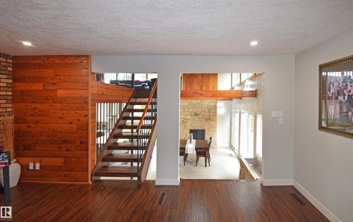 Wood-finish flooring, wood paneling, open staircase with metal spindles, recessed lighting, and a stone-faced fireplace - 9657 68A Street Nw, Edmonton, AB 