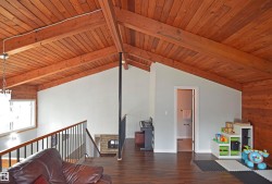Vaulted wood-paneled ceiling with exposed beams, wood-finish flooring, and a fireplace with stone surround - 