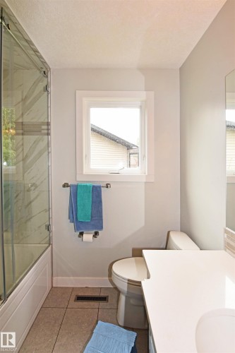 Tile flooring, white window trim, built-in tub with glass enclosure, single vanity with integrated sink, and white countertop - 9657 68A Street Nw, Edmonton, AB 