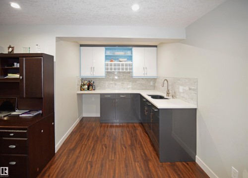 Wet bar featuring wood-finish flooring, white countertops, built-in cabinetry, and a tile backsplash - 9657 68A Street Nw, Edmonton, AB 
