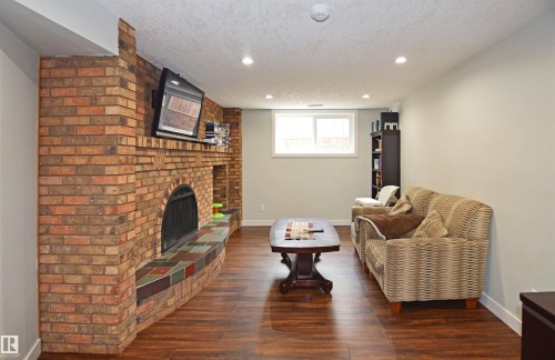 Wood-finish flooring with a brick fireplace featuring a tiled hearth - 9657 68A Street Nw, Edmonton, AB 