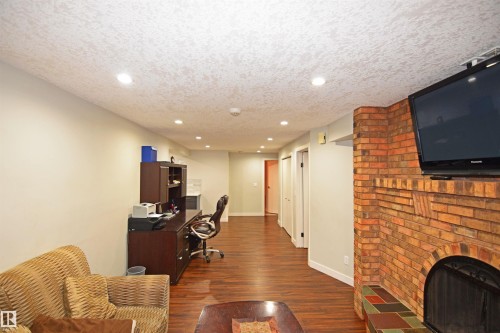 Recessed lighting illuminates the space, featuring wood-finish flooring and a brick fireplace with a tiled hearth - 9657 68A Street Nw, Edmonton, AB 