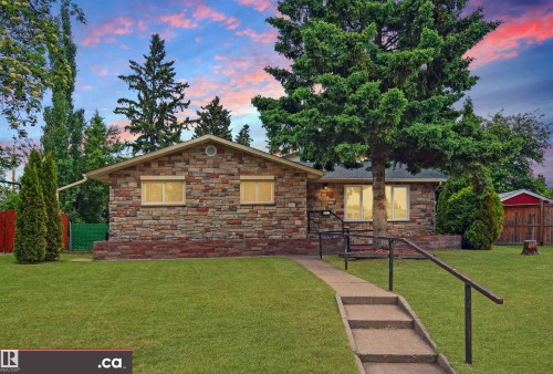 Stone veneer exterior, manicured front lawn, mature evergreen trees, concrete pathway, and a red garden shed - 9657 68A Street Nw, Edmonton, AB 