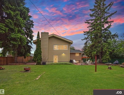 Spacious backyard featuring a manicured lawn, established mature trees, a privacy fence, and a paver patio area - 9657 68A Street Nw, Edmonton, AB 