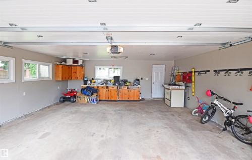 Attached two-car garage with concrete flooring, multiple windows, built-in wood cabinetry, and overhead lighting - 9657 68A Street Nw, Edmonton, AB 