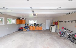 Attached two-car garage with concrete flooring, multiple windows, built-in wood cabinetry, and overhead lighting - 