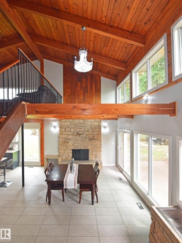 Vaulted wood-paneled ceiling with exposed beams, crystal chandelier, stone fireplace, tile flooring, and a wall of windows - 9657 68A Street Nw, Edmonton, AB 