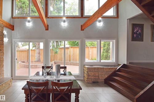 Vaulted ceiling with exposed wood beams, bright interior lighting, large windows, sliding glass door access to a brick paver patio, and wood-finish stairs - 9657 68A Street Nw, Edmonton, AB 