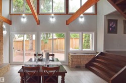 Vaulted ceiling with exposed wood beams, bright interior lighting, large windows, sliding glass door access to a brick paver patio, and wood-finish stairs - 