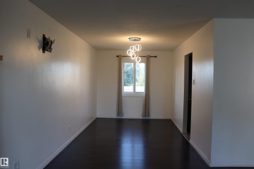 Dark wood-finish flooring, white walls, modern ceiling-mounted light fixture, window with drapes - 8828 151 Avenue Northwest, Edmonton, AB 