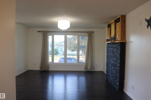 Dark wood-finish flooring, recessed window with white trim, and a stone-clad fireplace with wood detailing - 8828 151 Avenue Northwest, Edmonton, AB 
