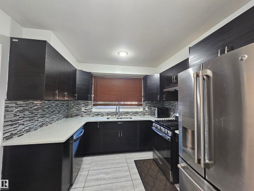 Modern kitchen featuring dark wood-finish cabinetry, light stone-finish countertops, and a full tile backsplash - 8828 151 Avenue Northwest, Edmonton, AB 
