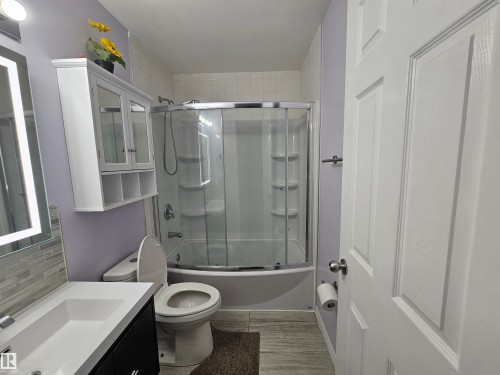 Wall-mounted vanity with integrated sink, modern illuminated mirror, tiled backsplash, and built-in medicine cabinet - 8828 151 Avenue Northwest, Edmonton, AB 