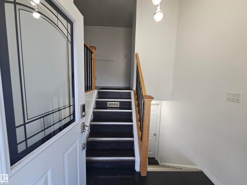 Entryway featuring a decorative glass door, a staircase with dark treads and a wood handrail, and white walls - 8828 151 Avenue Northwest, Edmonton, AB 
