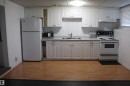 Kitchen featuring white shaker-style cabinetry, a white tile backsplash, light-toned wood-finish flooring, a stainless steel sink, and white appliances - 8828 151 Avenue Northwest, Edmonton, AB 