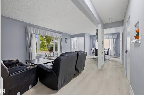 Light wood-finish flooring throughout, bright window with drapes, and an open layout with structural pillar - 13024 Sherbrooke Avenue Nw, Edmonton, AB 