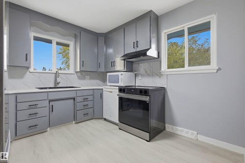 Kitchen featuring gray cabinetry, light-toned wood-finish flooring, white countertops, and a tile backsplash - 13024 Sherbrooke Avenue Nw, Edmonton, AB 