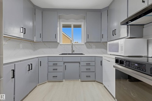 Kitchen featuring light gray cabinetry, white countertops, marble-look backsplash, and wood-finish flooring - 13024 Sherbrooke Avenue Nw, Edmonton, AB 
