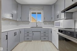 Kitchen featuring light gray cabinetry, white countertops, marble-look backsplash, and wood-finish flooring - 