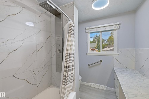 Bathtub with a multi-function shower panel, marble-look tile surround, and a coordinating marble-look vanity countertop - 13024 Sherbrooke Avenue Nw, Edmonton, AB 